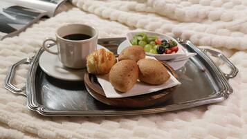 A tray with a cup of coffee, pastries, and a bowl of fruit on a bed.
