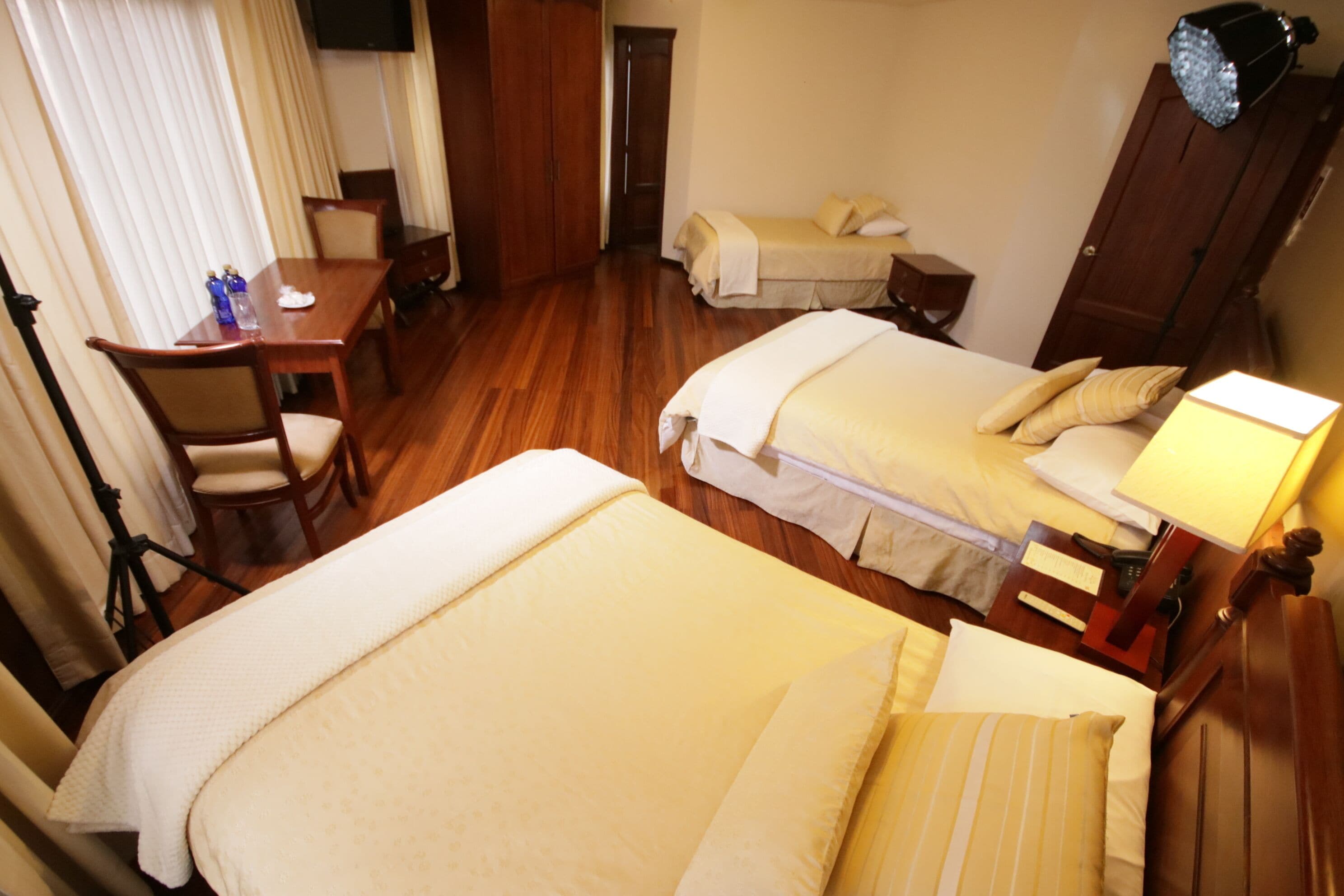 Habitación de hotel con dos camas, un escritorio con sillas, un televisor y una lámpara.