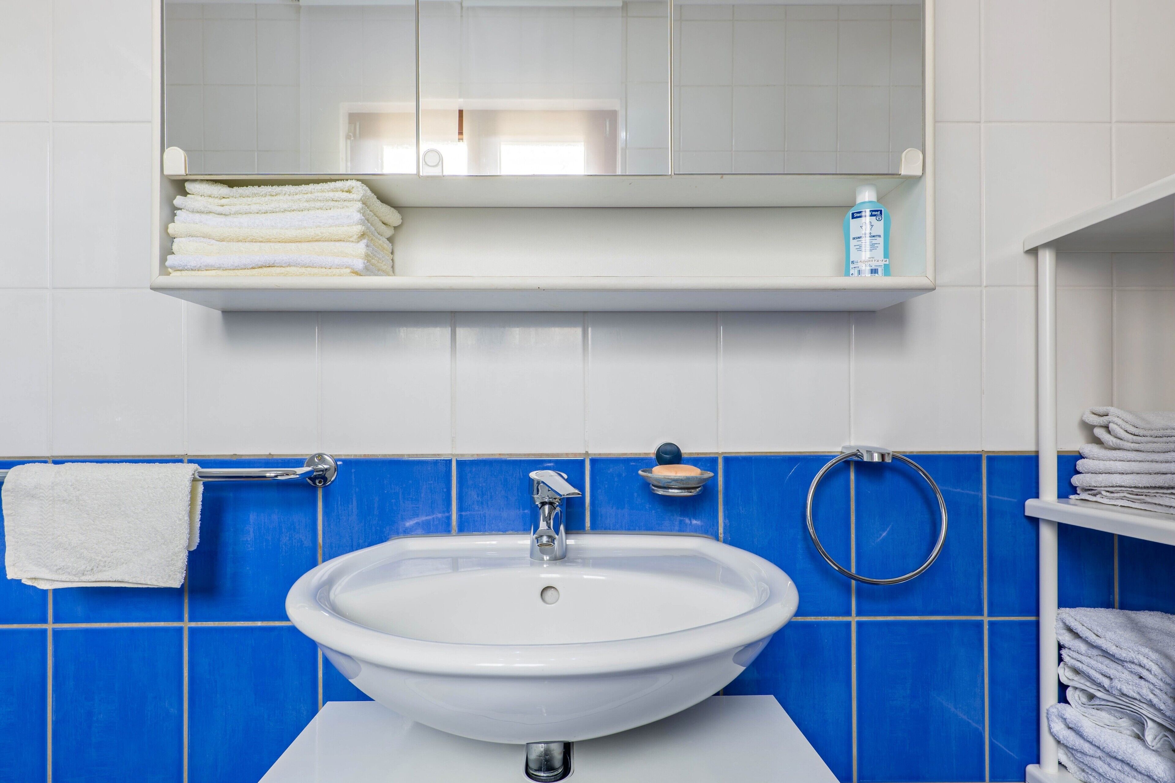 A bathroom with a white sink, blue tiles, a mirror, and a towel rack.