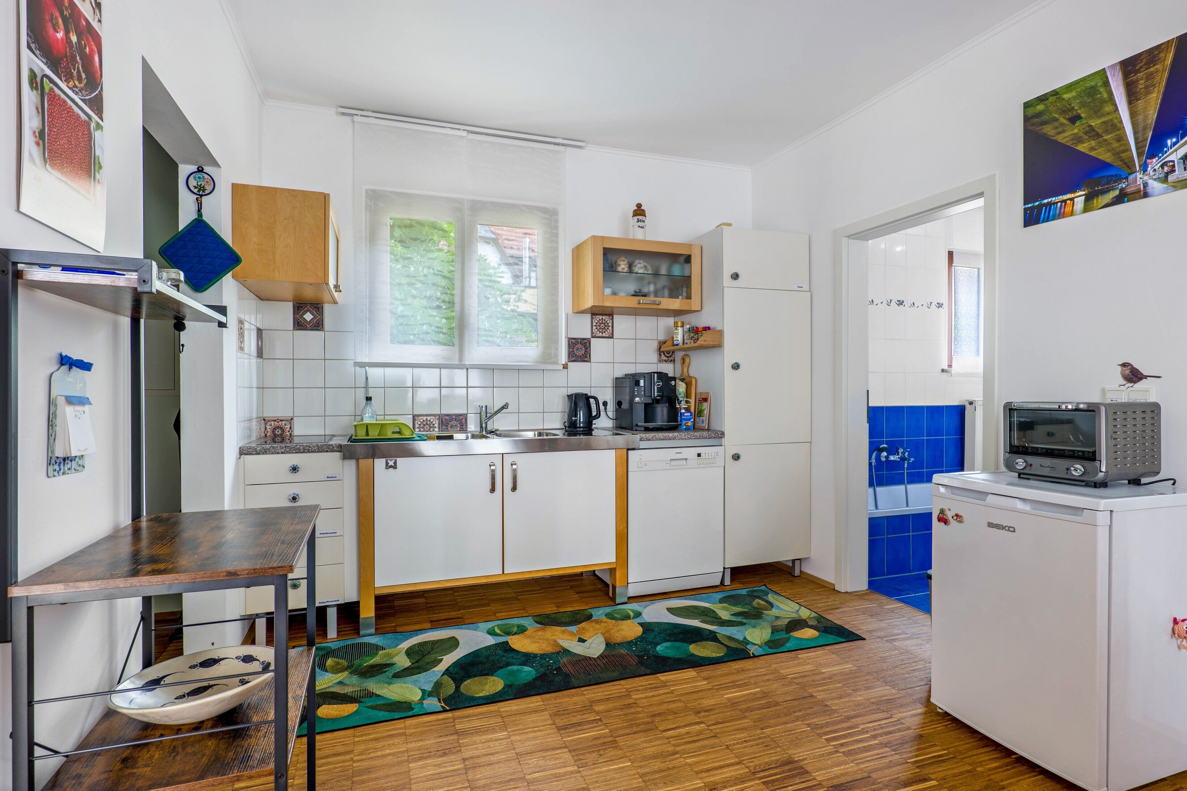 Een kleine keuken met witte kasten, een inbouwvaatwasser en een magnetron op een witte minibar.