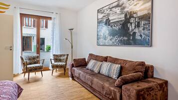Een woonkamer met een bruine bank, gestreept fauteuils, een vloerlamp en een groot zwart-wit landschap op de muur.