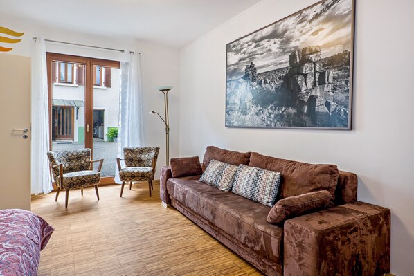 A living room with a brown sofa, patterned armchairs, a floor lamp, and a large black and white landscape painting on the wall.