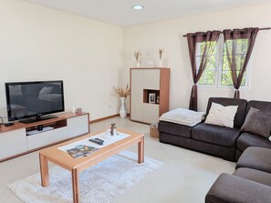 Ein modernes Wohnzimmer mit Flachbildfernseher, Couch, Holztisch und Schrank.