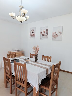 Comedor con una mesa dispuesta para cuatro personas, sillas de madera, un florero con flores secas y decoración en la pared.