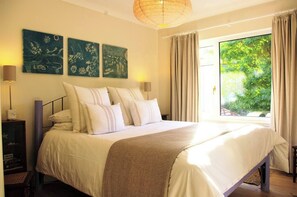 A bedroom with a large bed, a nightstand, a lamp, and a view of greenery outside. - Abbotscot near Bantham, S. Devon (West Buckland, Bantham)