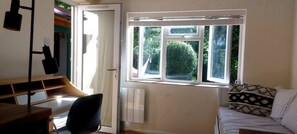 Ein Zimmer mit Schreibtisch, Stuhl und einem Bett mit gemusterten Kissen.