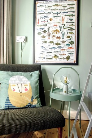 Ein Zimmer mit einer an der Wand befestigten Übersicht über Fische und Meeresfrüchte, einer Lampe auf einem kleinen Tisch und einem gemusterten Kissen auf einem Sofa.