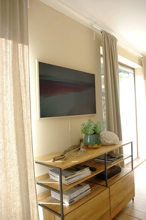 A room with a mounted flat-screen TV, a wooden console table with books and decorative items, and a window with curtains. - Abbotscot near Bantham, S. Devon (West Buckland, Bantham)