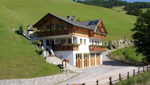 Ein zweistöckiges Holzhaus mit einem Balkon, einer Steinmauer und einem gepflasterten Auffahrt.