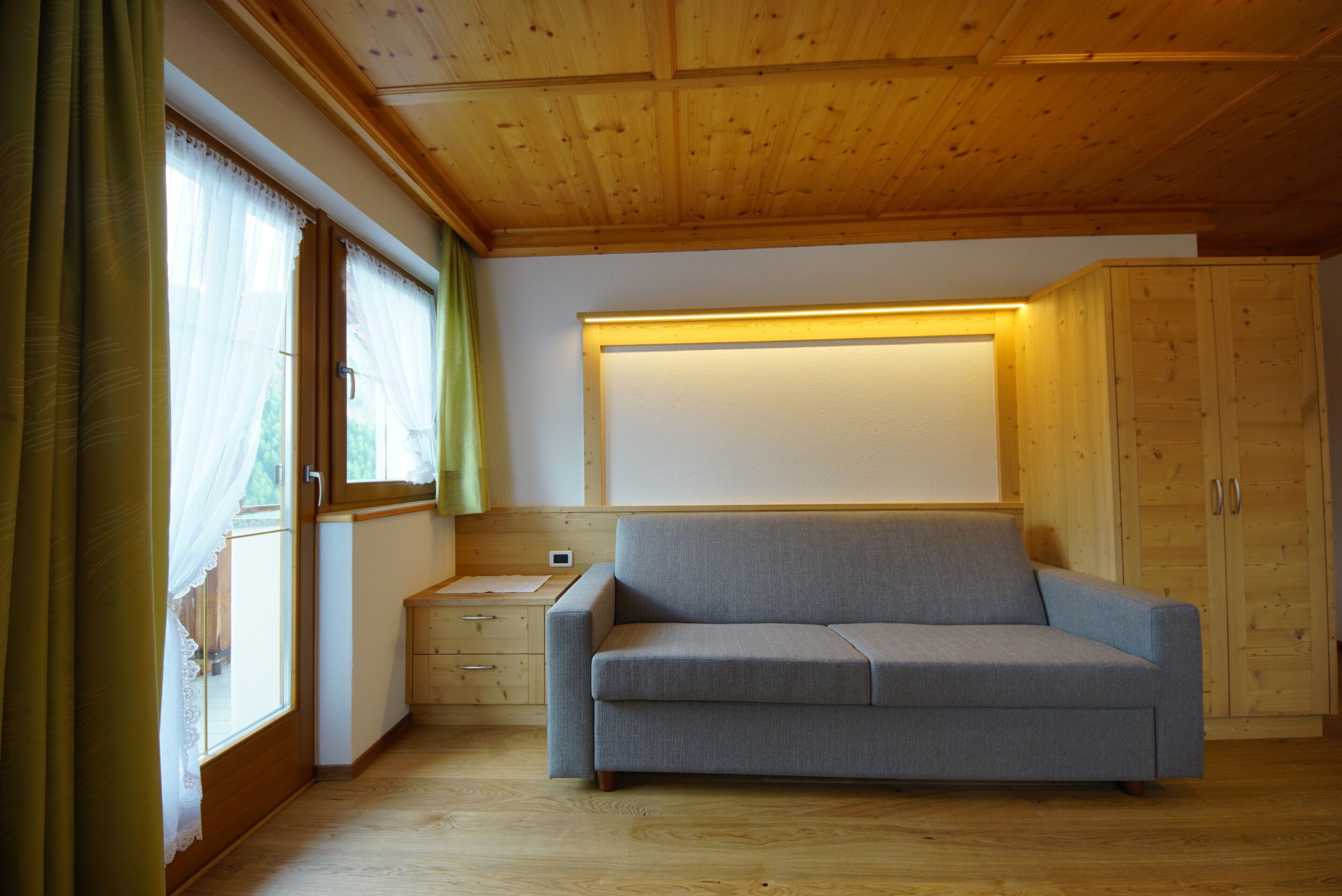 Une pièce avec un plafond en bois, un canapé gris, un meuble en bois et une fenêtre avec des rideaux.