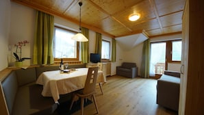 Ein gemütliches Zimmer mit Esstisch, Bank, Fernseher und einer Couch.