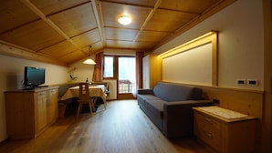 A compact room with a wooden ceiling, a sofa, a dining table with chairs, a television, and a small cabinet. - Apartment 'Agriturismo Grones' with Mountain View, Shared Terrace and Wi-Fi (San Martin de Tor)