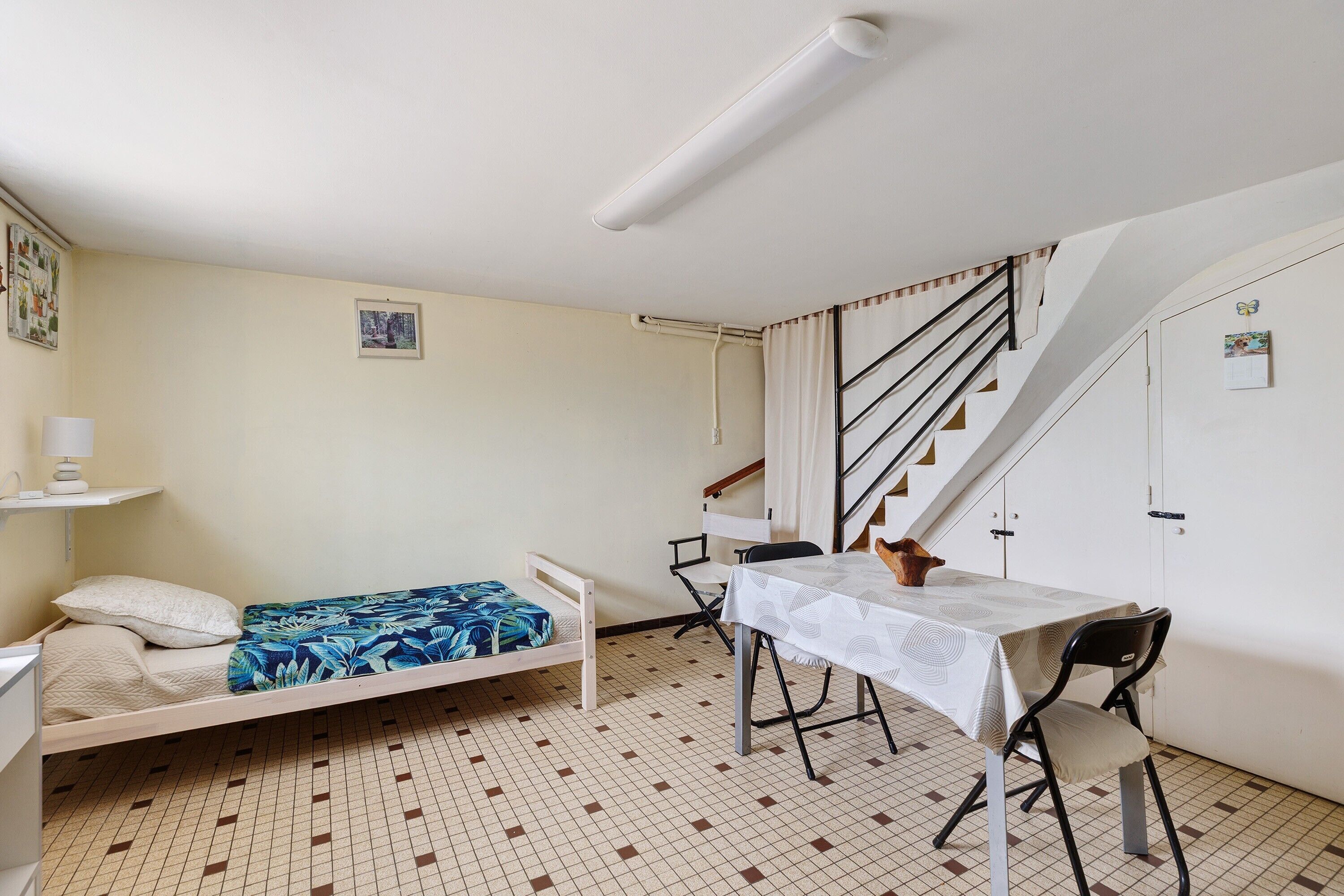 Una stanza piccola e funzionale con un letto, un tavolo e una sedia. Si vede una scala che conduce a un piano superiore.