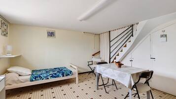 Una stanza piccola e funzionale con un letto, un tavolo e una sedia. Si vede una scala che conduce a un piano superiore.