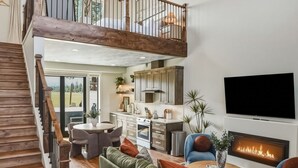 A spacious living area with a wooden staircase, a fireplace, and a TV mounted on the wall.