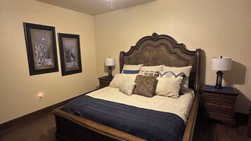 Quarto com cama de madeira, duas mesas de cabeceira com luminárias, um ventilador de teto e duas molduras com imagens na parede.
