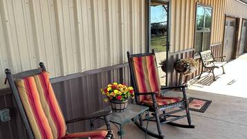A porch with two rocking chairs and a table, a potted plant, and a wooden building with vertical siding.