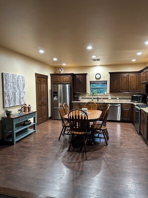 Una cocina con armarios de madera, un refrigerador de acero inoxidable, una mesa de comedor con sillas y un reloj en la pared.