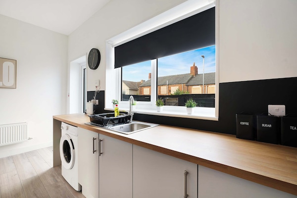 The kitchen features a dining table for four, fridge freezer, oven, hob, microwave, washing machine, and kitchenware. Tea, coffee, sugar, and a first aid kit are available, with access to the backyard.
