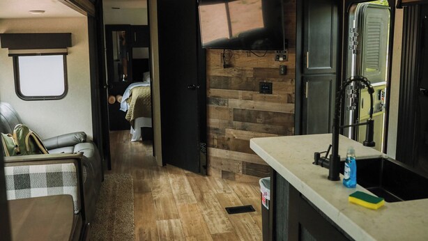 Interior compacto de una caravana con kitchenette, zona de estar y dormitorio.
