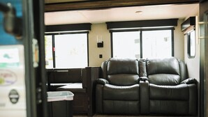 Interior de autocaravana con dos sillones de cuero reclinables, una mesita y una ventana con vistas al exterior.