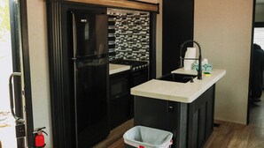 Una cocina compacta con refrigerador, estufa, lavamanos y un pequeño bote de basura.