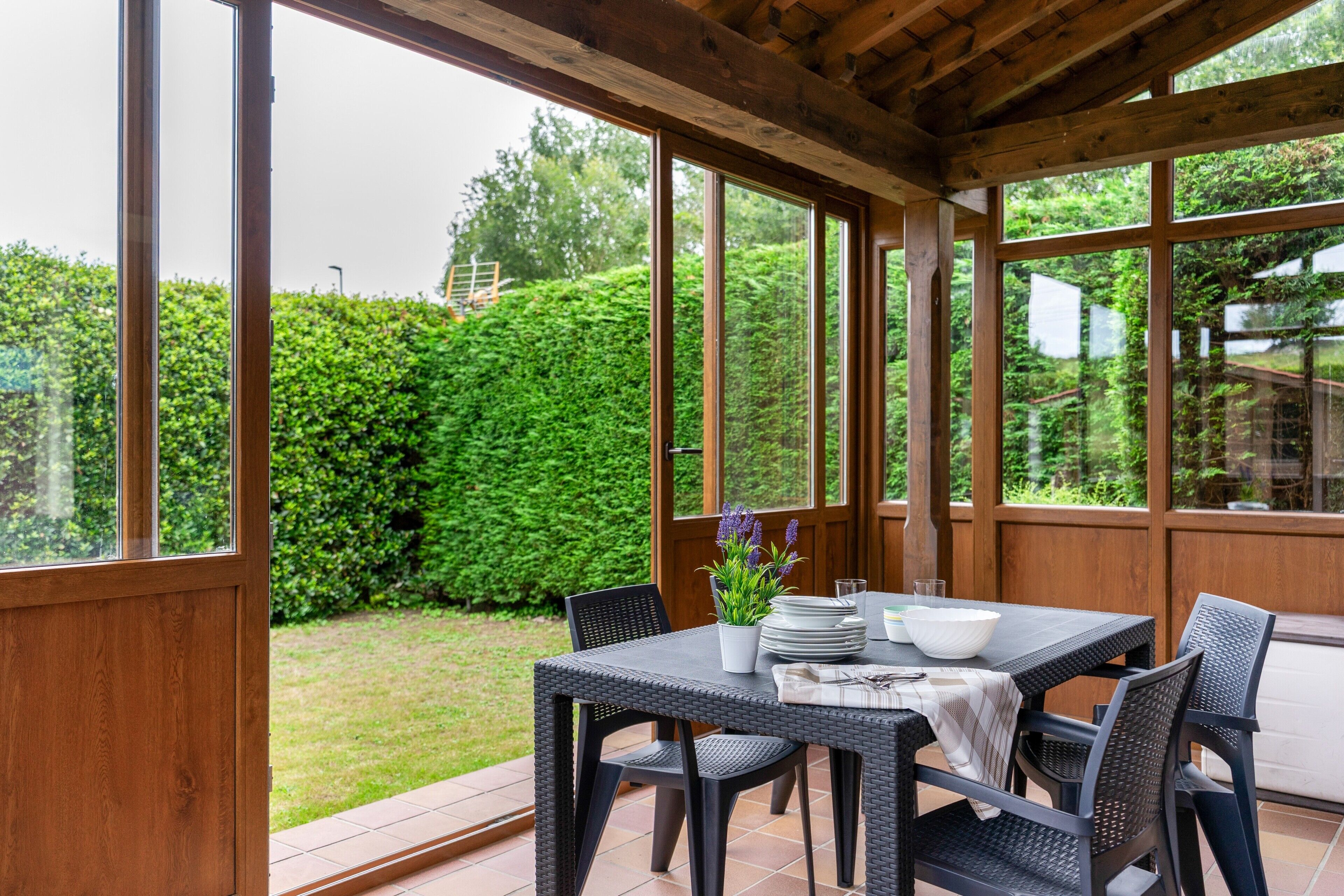 An outdoor patio with a table set for dining, surrounded by large windows and a wooden ceiling.