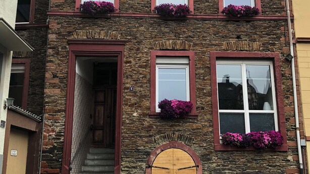 Een stenen gebouw met een houten deur, meerdere ramen met bloembakken en een schotelantenne.