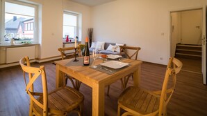 Een eetgedeelte met een houten tafel, vier stoelen, een fles wijn en een bloevas.