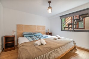 A bedroom with a large bed, a wooden headboard, a nightstand, a lamp, and a window with a view of a building. - Country House 'Bellpuig' with Mountain View, Wi-Fi and Air Conditioning (Artà)