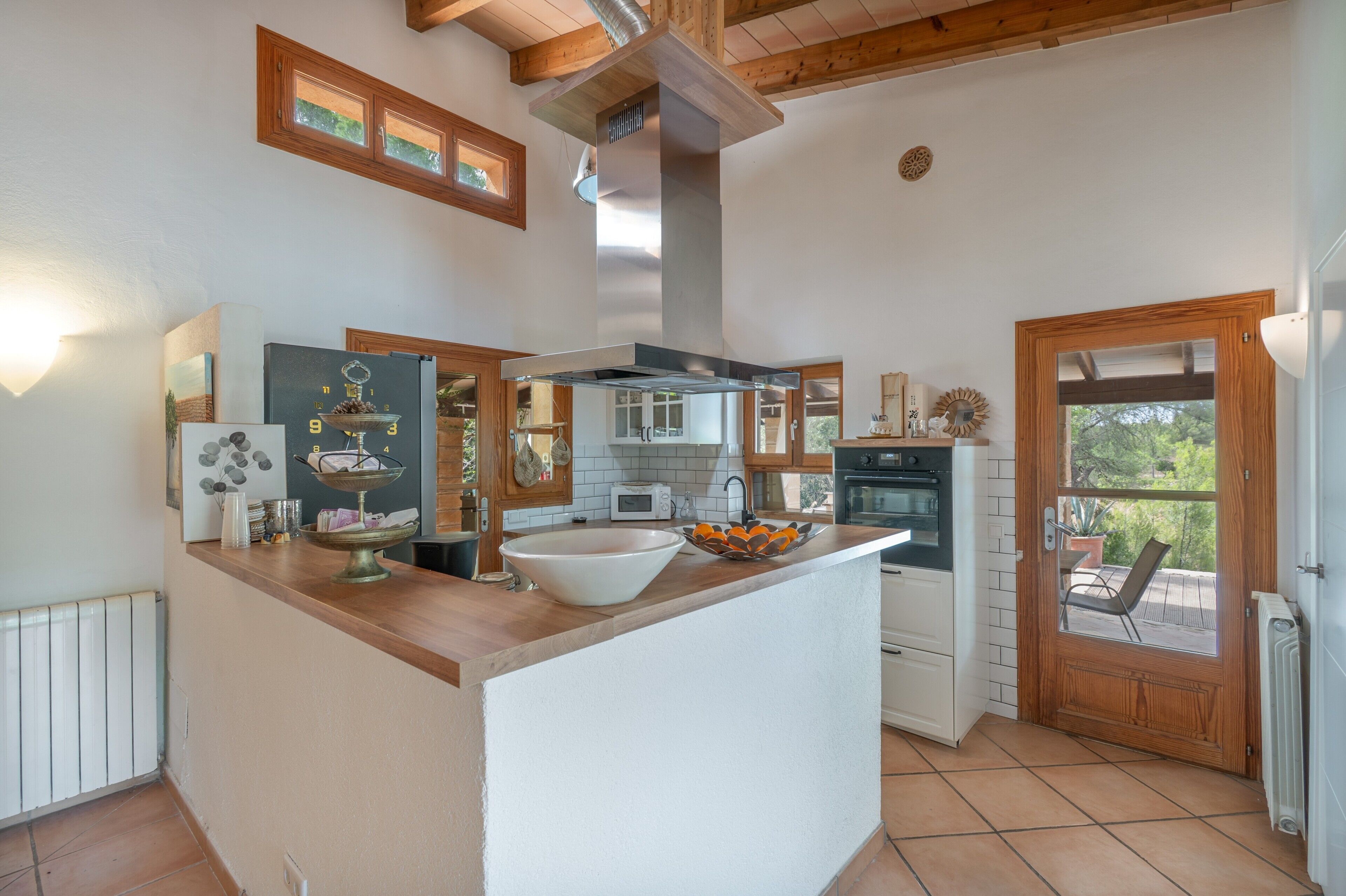 Cocina con isla central, armarios de madera, horno empotrado y vista a través de la puerta.