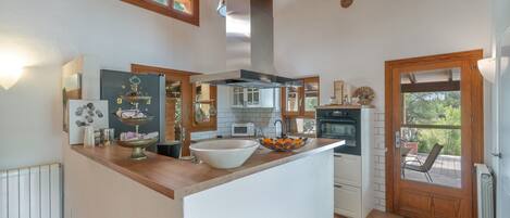 Cocina con isla central, armarios de madera, horno empotrado y vista a través de la puerta.