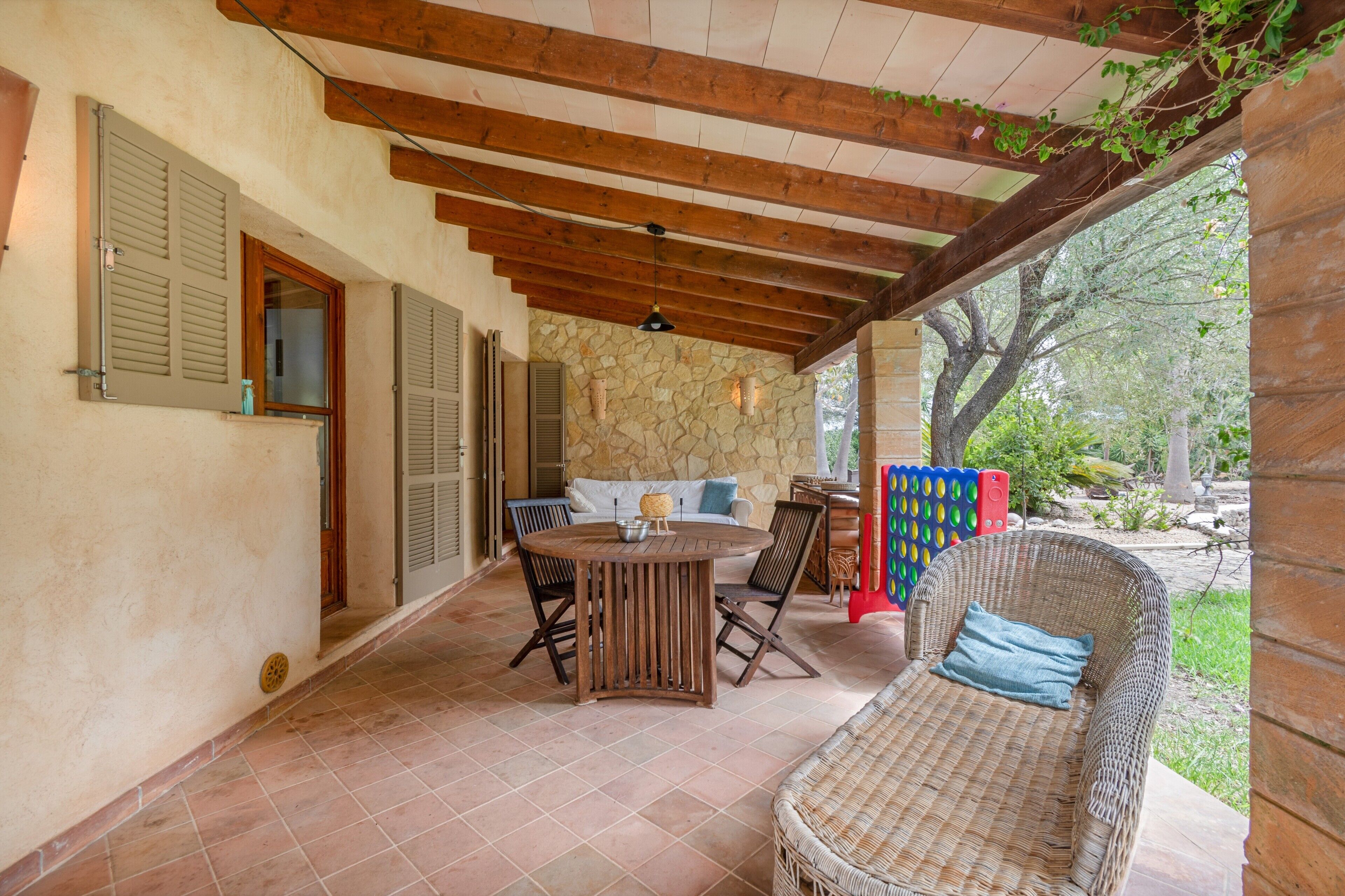 Un patio al aire libre con pared de piedra, vigas de techo de madera, una mesa redonda y mobiliario de mimbre.
