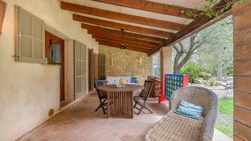 Un patio al aire libre con pared de piedra, vigas de techo de madera, una mesa redonda y mobiliario de mimbre.