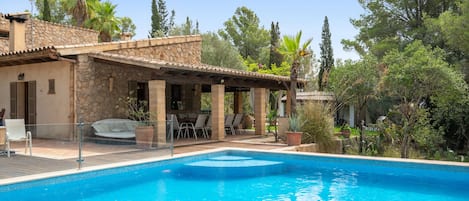 Propiedad residencial con piscina, mobiliario exterior y fachada de piedra.
