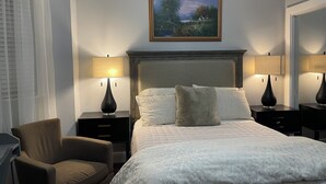 A bedroom with a bed, two bedside tables with lamps, a chair, a painting on the wall, and a window with curtains. - Modern 3BR Apartment Near NYC & Cruise Port (Bayonne)