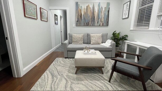A living room with a grey sofa, a coffee table, and a grey armchair. There is a painting on the wall and a plant on the side. - Modern 3BR Apartment Near NYC & Cruise Port (Bayonne)