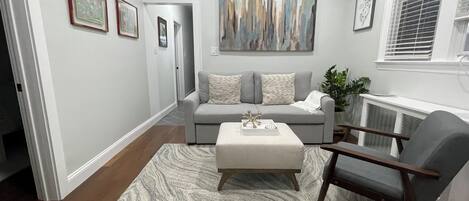 Sala de estar con un sofá gris, una mesa de centro y un sillón gris. Hay un cuadro en la pared y una planta al lado.
