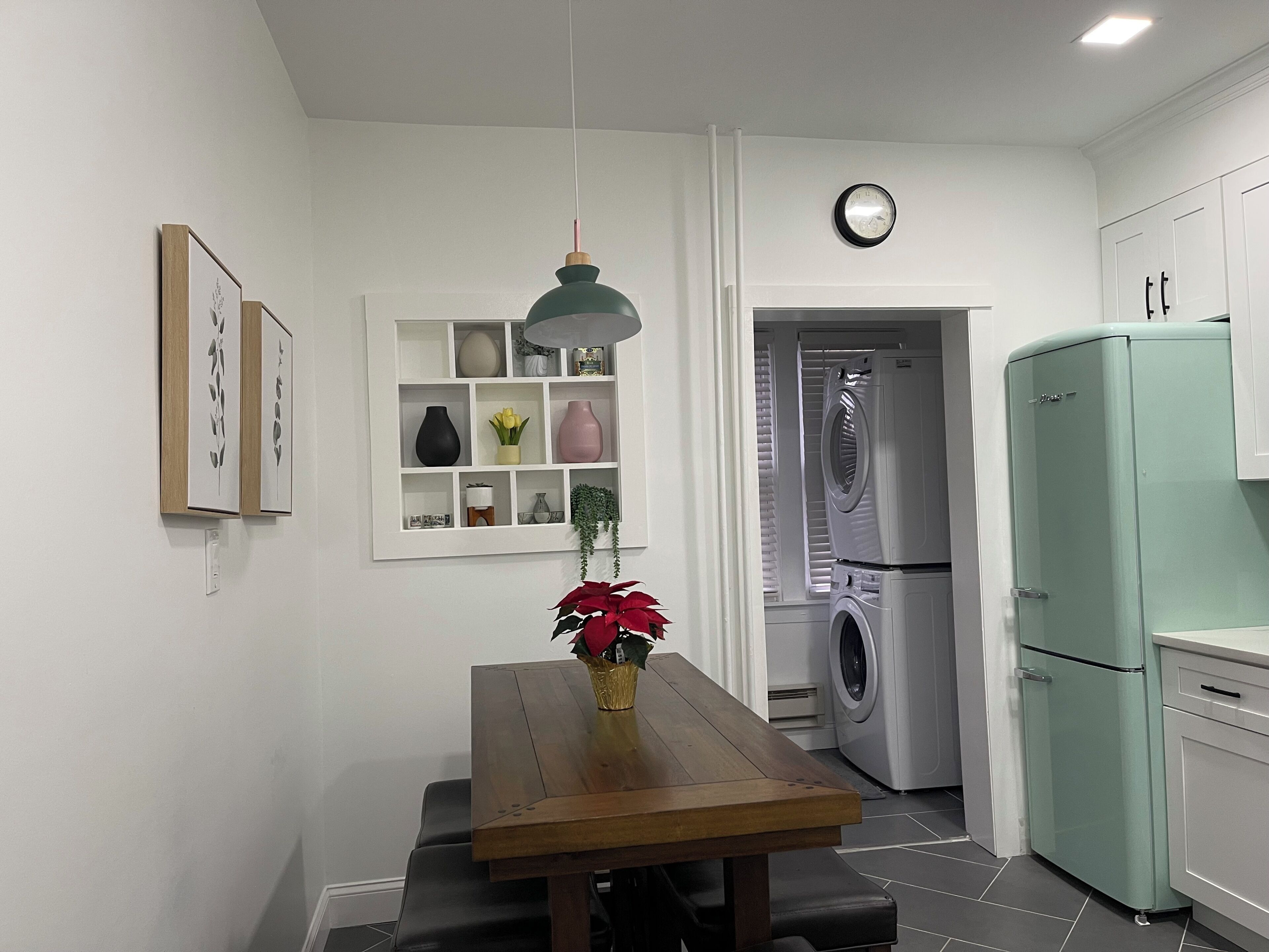 A kitchen with a dining table, a hanging light fixture, a clock, and a washing machine.
