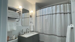 Une salle de bain comprenant des toilettes, un lavabo, un miroir, un porte-serviettes, un rideau de douche et un luminaire au plafond.