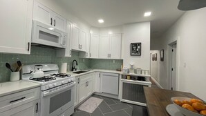 A modern kitchen with white cabinets, a gas stove, a microwave, and a coffee maker. - Modern 3BR Apartment Near NYC & Cruise Port (Bayonne)
