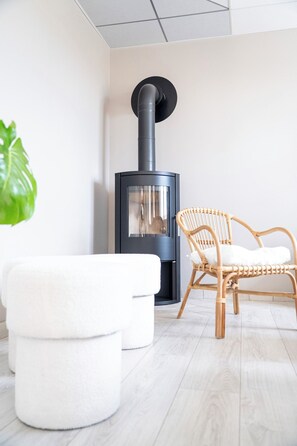 A modern interior with a wood-burning stove, a wicker chair, and a white ottoman. - Villa Josée – Renovated family home, 700 meters from the beach (Kerlouan)