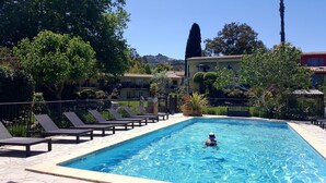 A swimming pool with lounge chairs, surrounded by greenery and buildings.