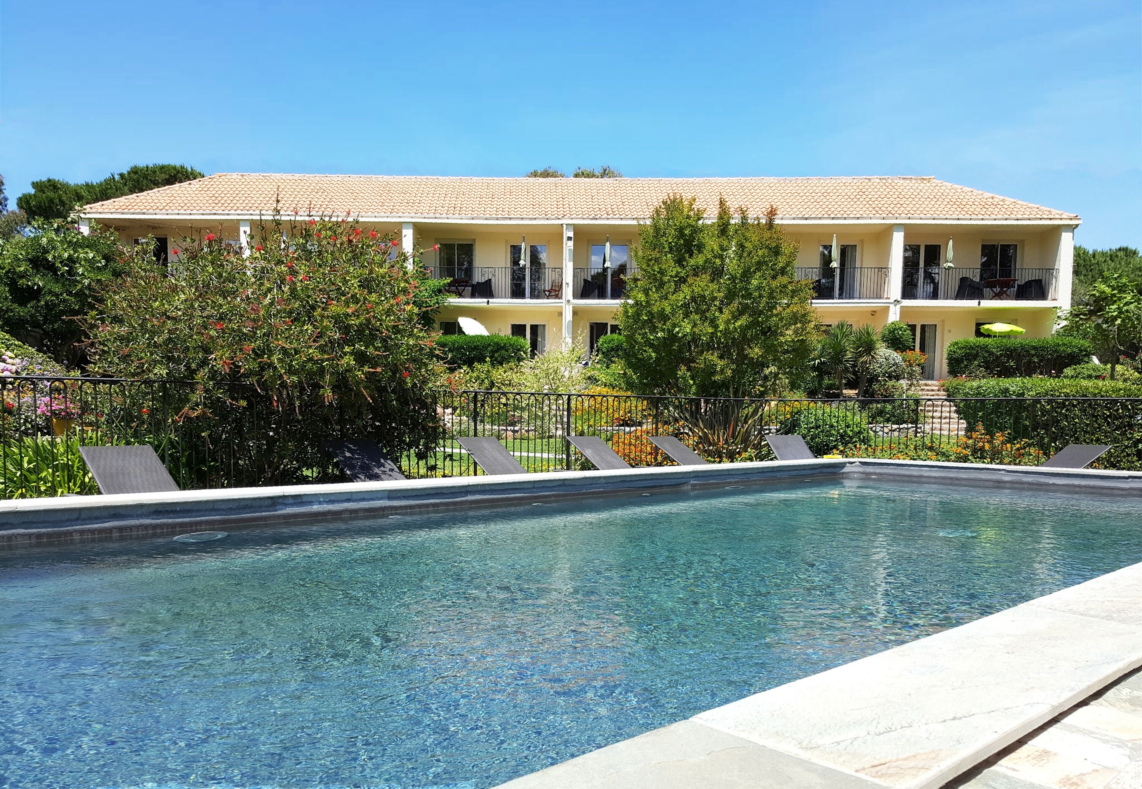 A pool area with lounge chairs, a building with balconies, and a clear blue sky.
