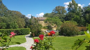 A garden pathway leading to a building with a tiled roof, surrounded by lush greenery and flowering plants.