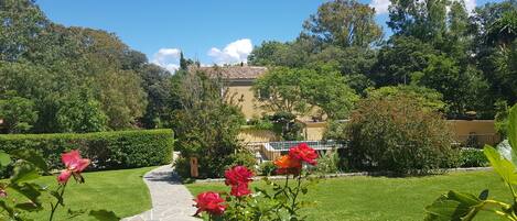 A garden pathway leading to a building with a tiled roof, surrounded by lush greenery and flowering plants.