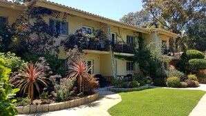 A two-story building with balconies, a well-maintained garden, and a clear sky.