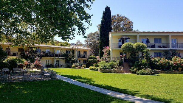 A two-story building with balconies, a well-maintained lawn, and a variety of plants.