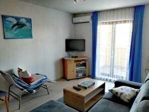 A living room with a TV, a sofa, a coffee table, a chair, and a window with curtains. - CASA Gabrijela - Bijou Apartment - Ideal for couples / couples with small children (Poreč)