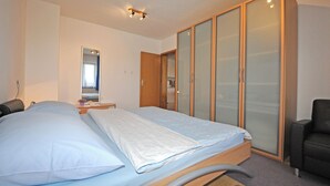 Ein Schlafzimmer mit zwei Betten, einem Kleiderschrank, einem Sessel und einem Spiegel.